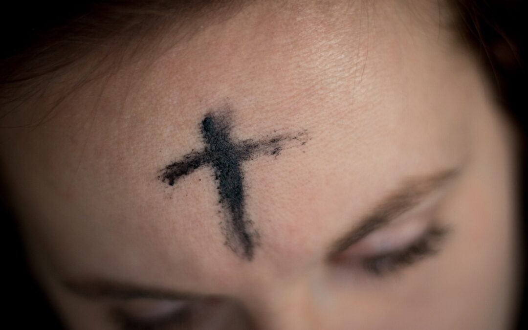 A black cross of ash dush on a woman’s forehead.