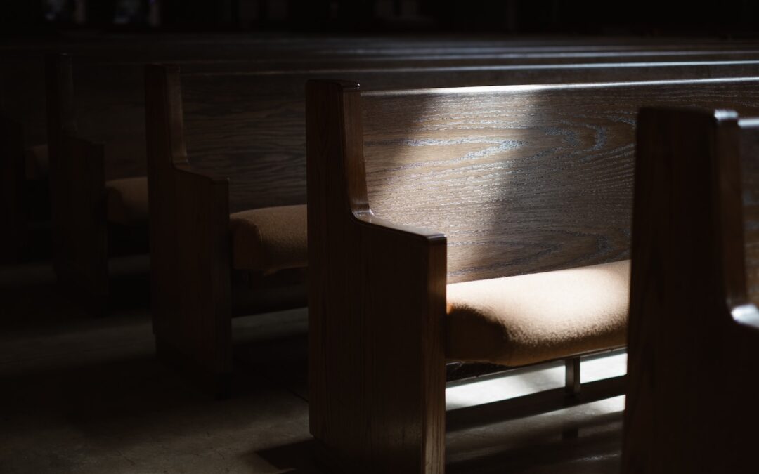 A row of church pews in a dark room with a single sunspot shining down.