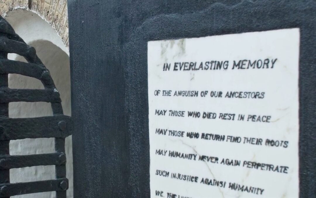 A white plaque with black lettering on a wall at a former slave castle in Ghana memorializing all who died in the transatlantic slave trade.