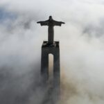 A statue of Jesus rising out of the fog view from above.