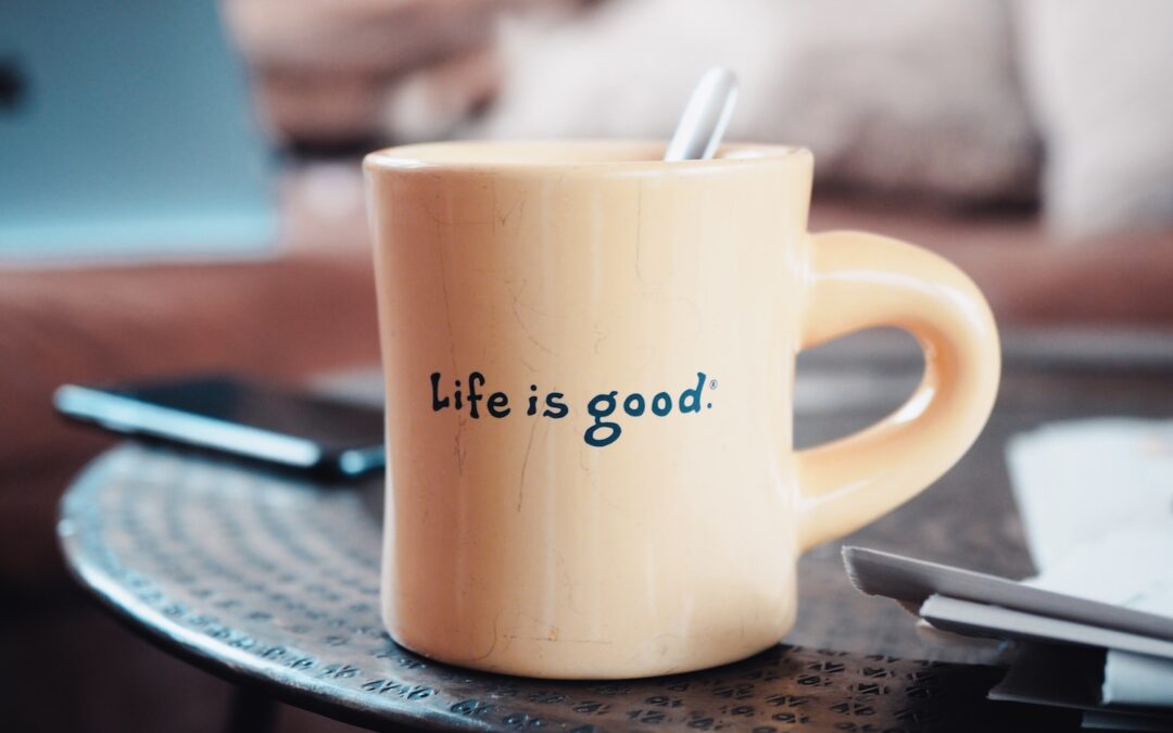 A coffee mug with the words “Life is Good” on the side sitting on a table.