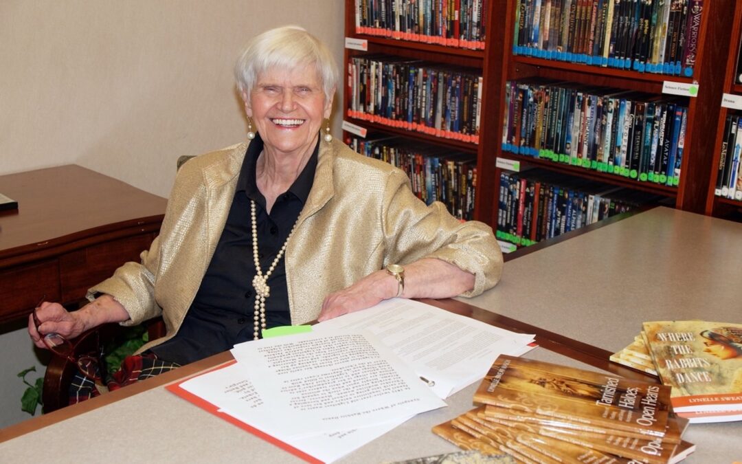 A woman smiling while sitting at a table with books on it.