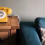 A yellow phone sitting on a side table next to a blue couch.