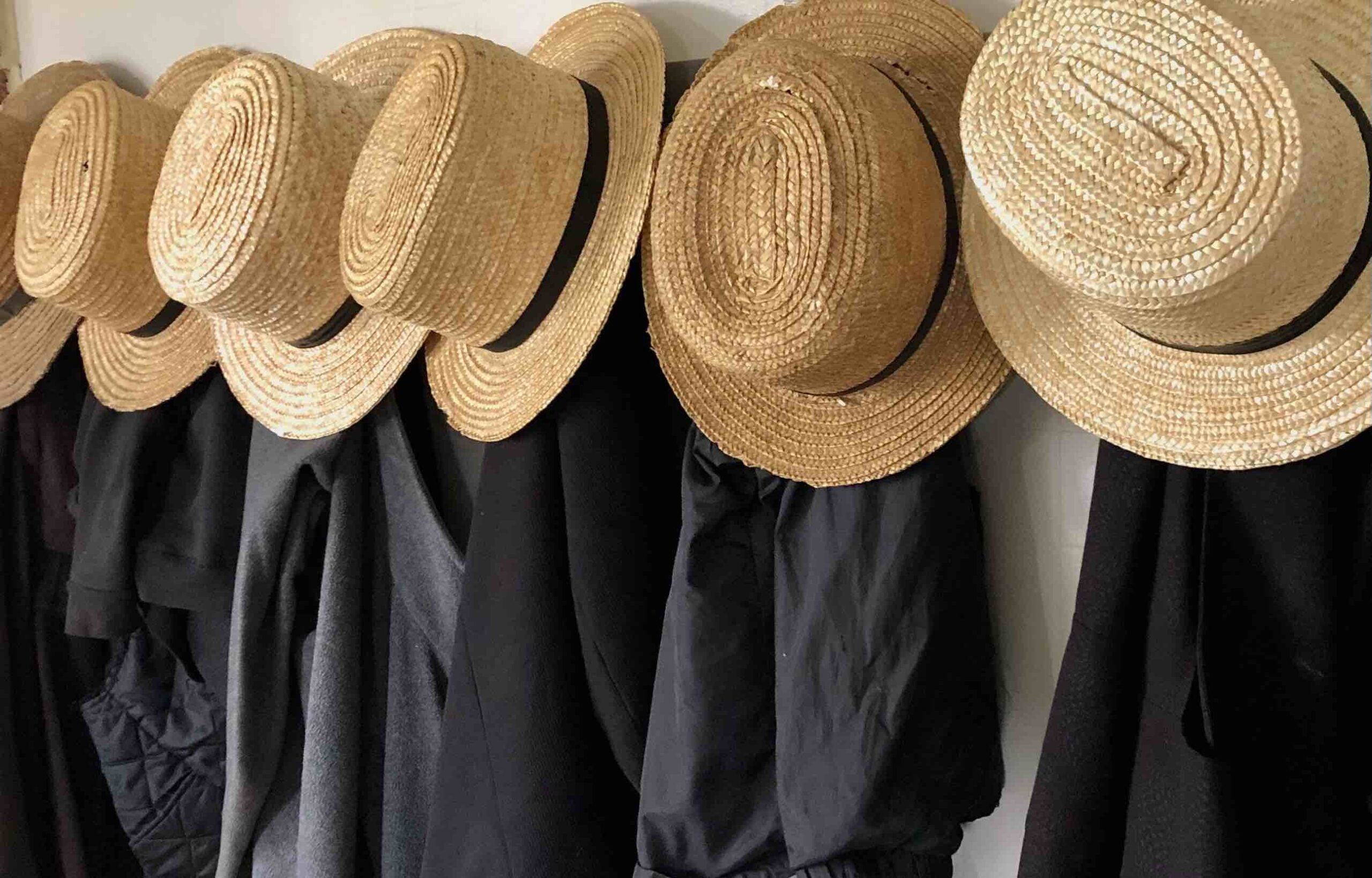 Amish clothing hanging in a row on a wall.