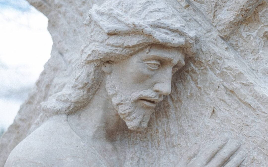 A closeup of a concrete statue of Jesus carrying a cross.