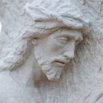A closeup of a concrete statue of Jesus carrying a cross.
