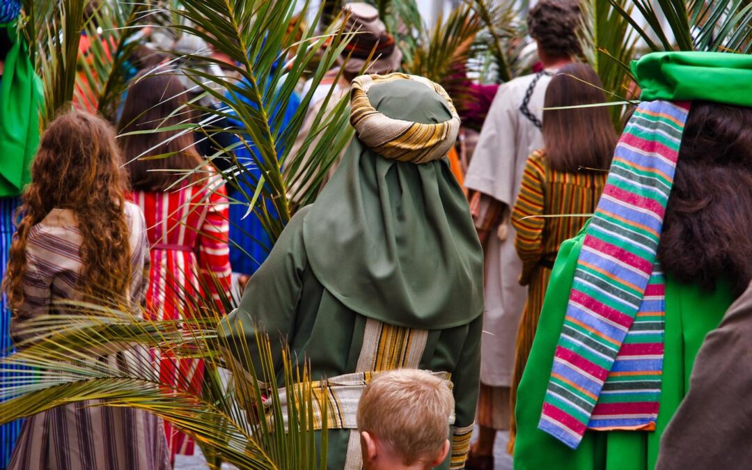 People seen from behind dressed in robes and carrying palm branches.
