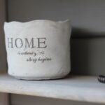 A wooden shelf with a pottery jar on it that says, “Home is where your story begins.”