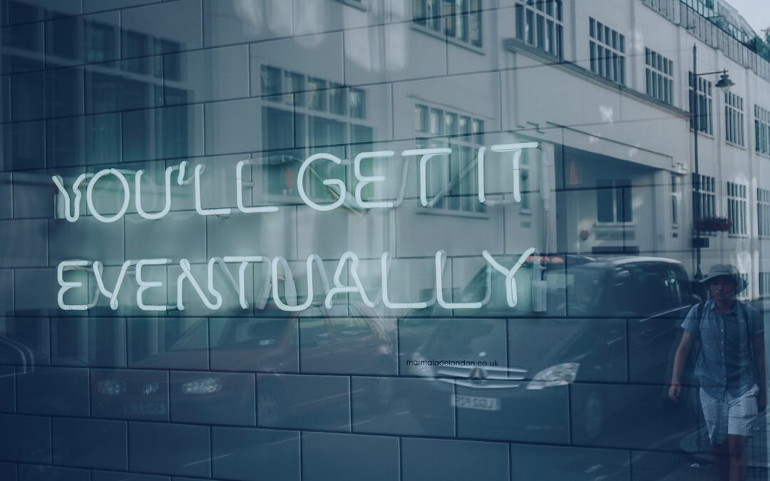 A large window on a street reflecting a neon sign that says, “You’ll get it eventually.”