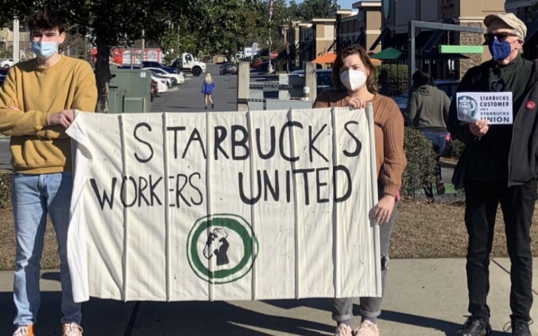 Starbucks employees on the street holding a sign that says, “Starbucks Workers United.”
