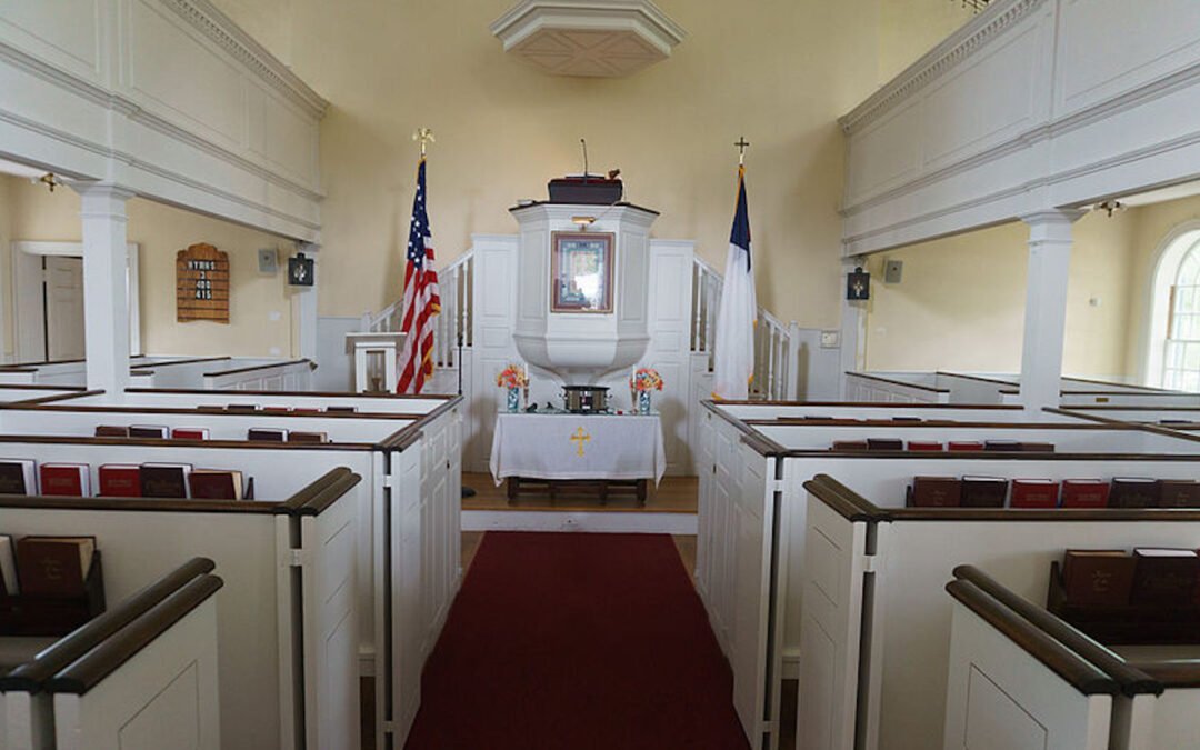 The interior of a church sanctuary featuring a U.S. flag on one side of the communion table and a Christian flag on the other.