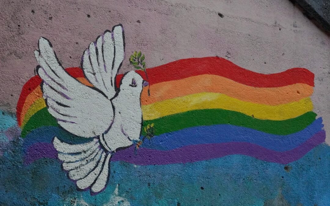 A wall mural of a pride flag and a white dove holding sprigs of greenery in its beak and feet.