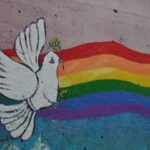 A wall mural of a pride flag and a white dove holding sprigs of greenery in its beak and feet.