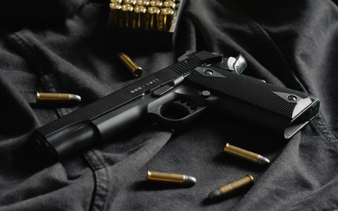 A handgun on a table with bullets around it.