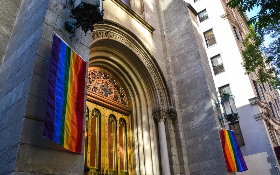 Two rainbow-colored flags on either side of the doors to a church.