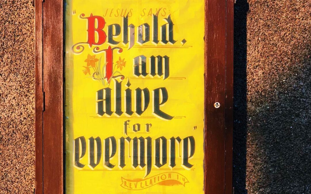 A church sign with a yellow background and red and black text with the words, “Jesus says, ‘Behold, I am alive for evermore.’”