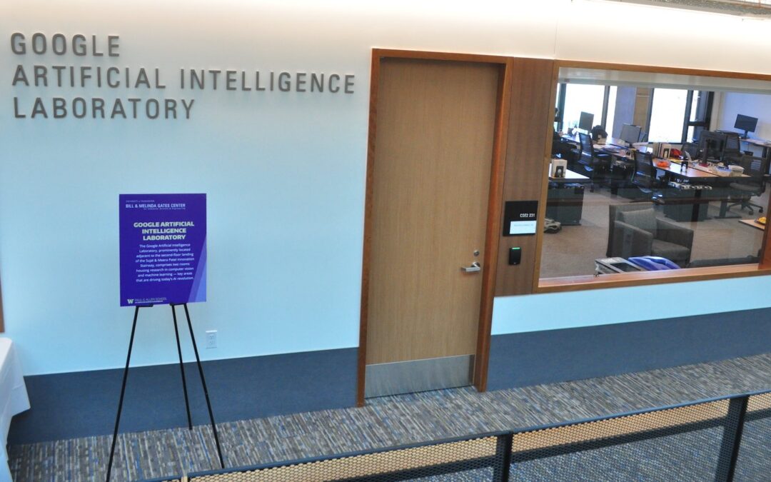 An office hallway, with a window looking into a room with desks and computers, and with a sign on the outside that says, “Google Artificial Intelligence Laboratory.”