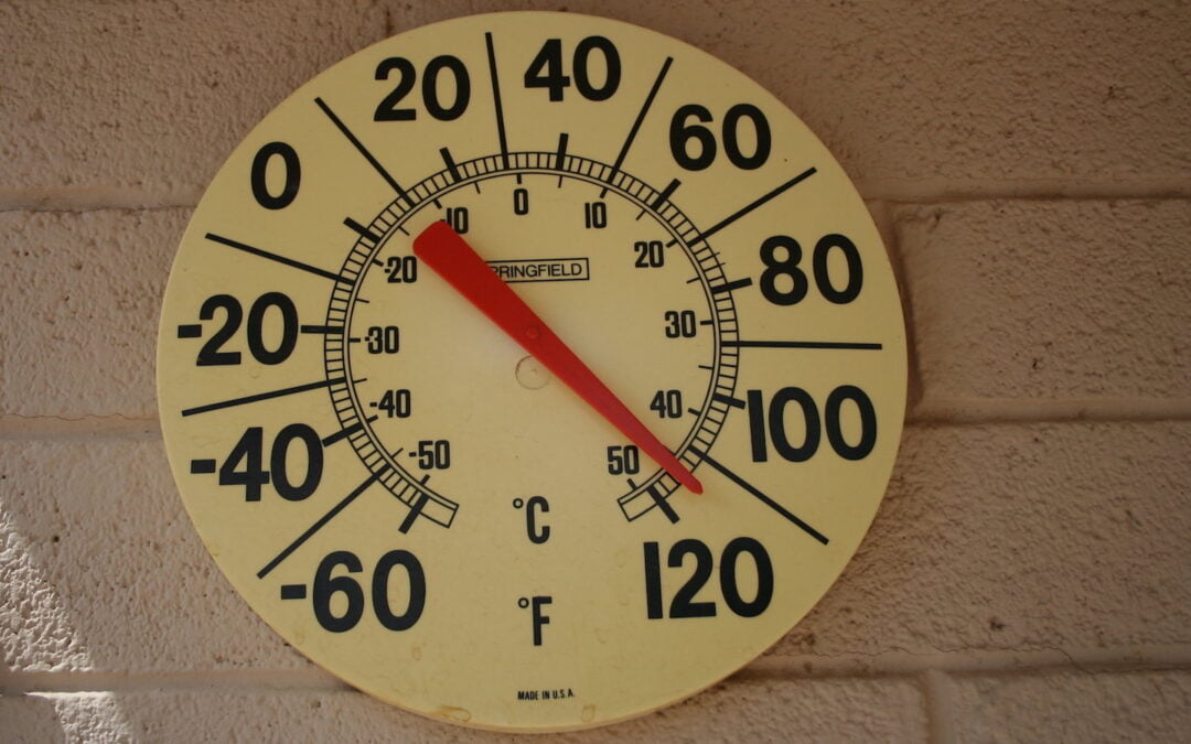 A round outdoor thermometer mounted on a brick wall.