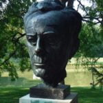 A metal bust of theologian Paul Tillich on a concrete base with a river or pond in the background.