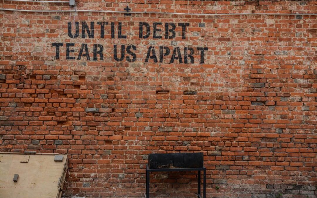 A red brick wall with the words “Until Debt Tear Us Apart” in black lettering on it.