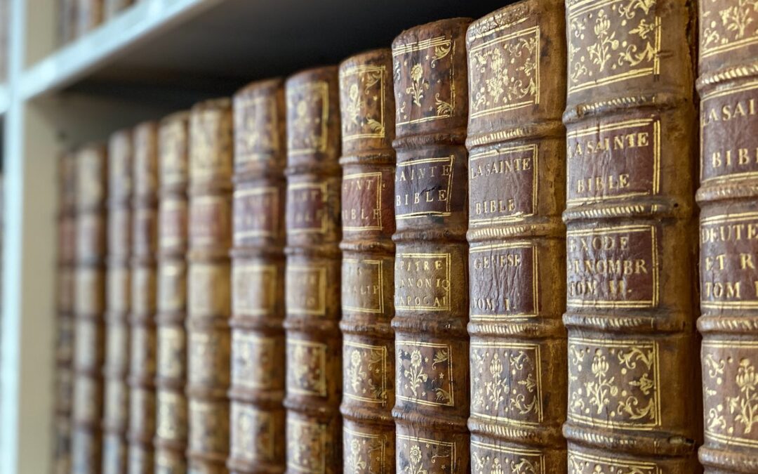 A row of antique books related to the Bible on a bookshelf.