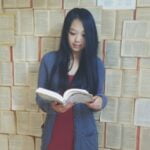 A girl holding a book standing in front of wallpaper that looks like open books.