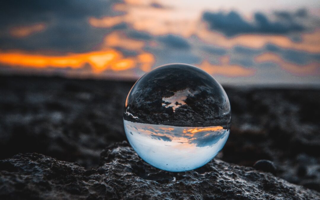 A clear crystal globe sitting on rocks with the sun setting in the background.
