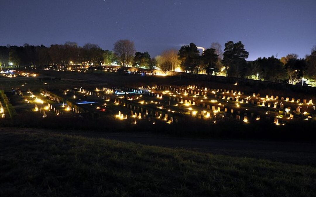 Candles across a cemetery at night for an All Saints’ Day commemoration.