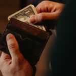 A person pulling some money out of a brown, leather wallet.