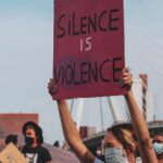 A woman holding a sign that says, “Silence is violence.”