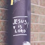 The statement, “Jesus is Lord,” written on a black pole standing next to a red brick wall.