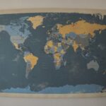 A world map painted on a canvas that is hung on an off-white wall.