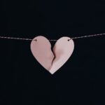 A pink heart hanging on a string with a crack down the middle.