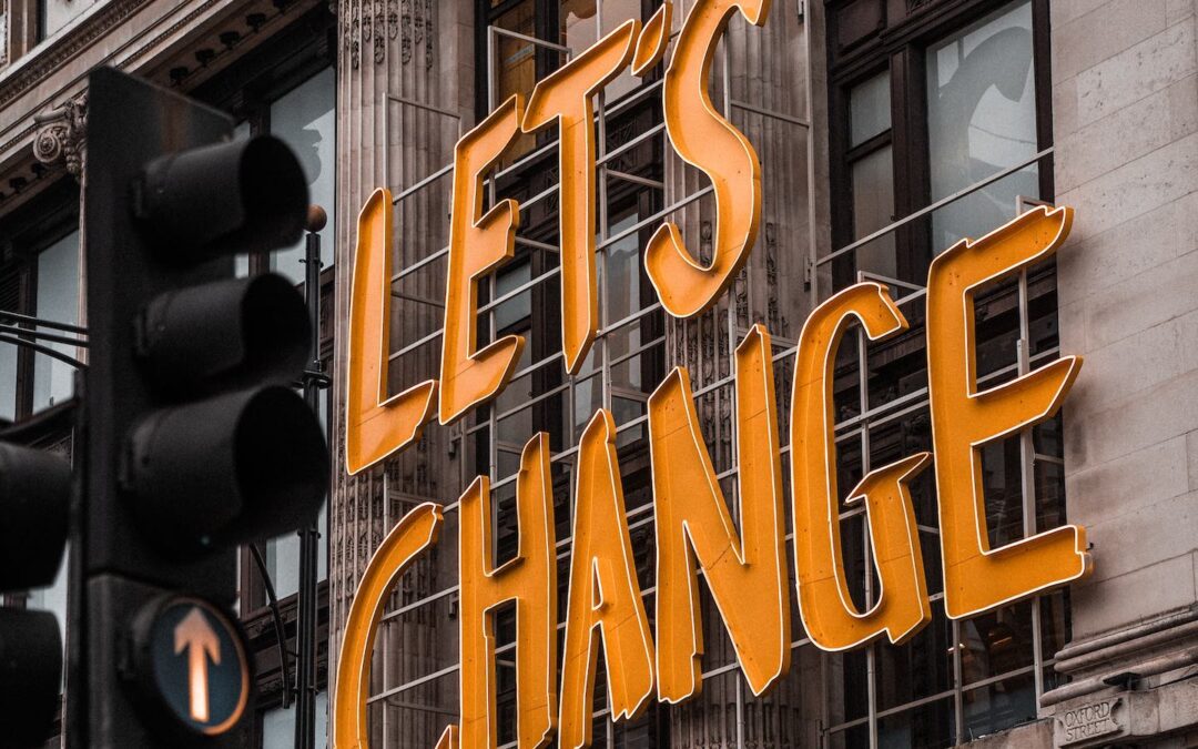 A yellow, metal sign on the sign of a brick building that says, “Let’s Change.”
