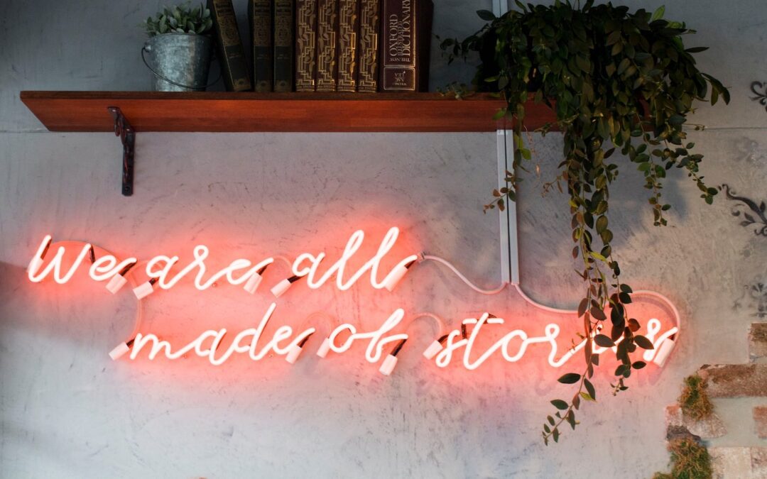 A pink, neon sign on a wall that says, “We are all made of stories.”