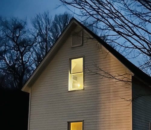 The exterior of the house in the early evening with a candle illuminating the window.