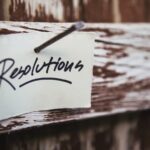 : A white notecard with the word, “Resolutions” written on it, nailed to a wooden fence.