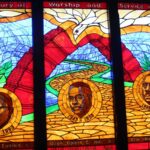 A stained-glass window in Howard University chapel featuring (left to right) Deans Evans E. Crawford Jr, Daniel C. Hill Jr, and Howard W. Thurman.