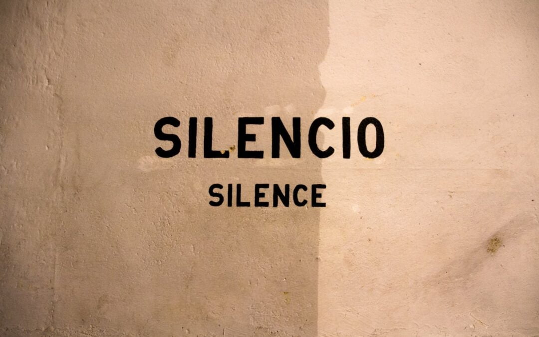 The words “silencio” and “silence” written on a stucco wall.