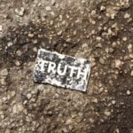 A black-and-white sign with the word “truth” on it lying on a sidewalk.