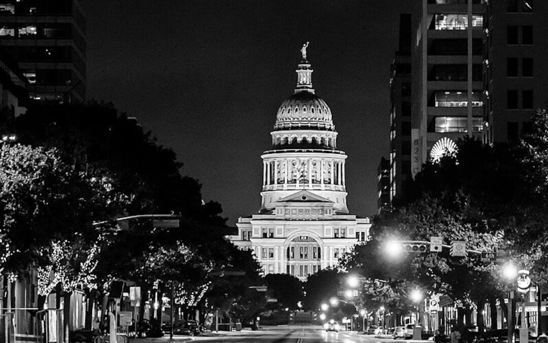 The exterior of the Texas Capitol illuminated a night in a black-and-white photo.