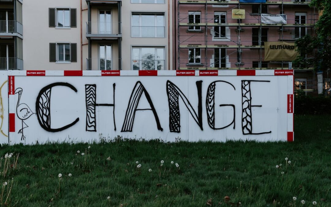 A white concrete wall on which the word “change” is spray painted.