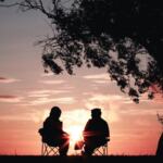 The silhouette of two people sitting outside talking.