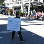 A woman holding a sign that reads, “LGBTQ+ kids have a right to be safe at school.”