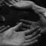 A grayscale photo of several hands outstretched.