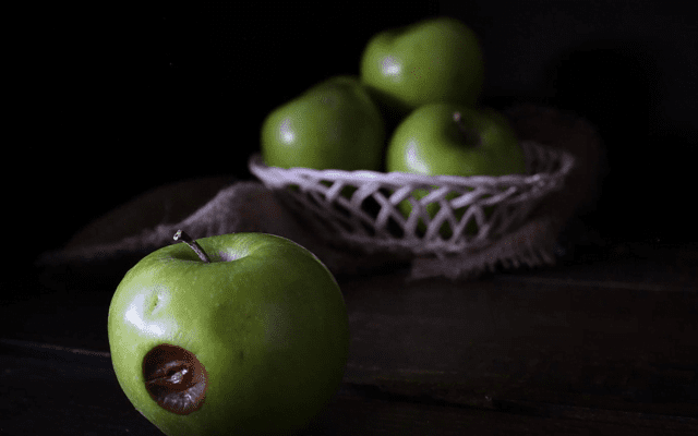 One rotten apple alongside a basket of apples.