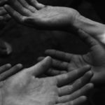 A black and white image of multiple pairs of hands extended, palms facing upward.