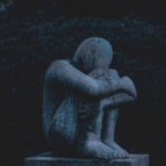 A stone sculpture of a person hugging his knees in grief.