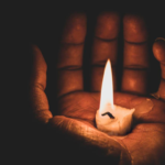 A grayscale photo of a candle in the palm of a person’s hand.