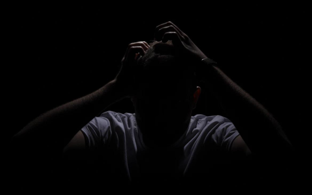 Man sitting in the dark with his hands in his hair.